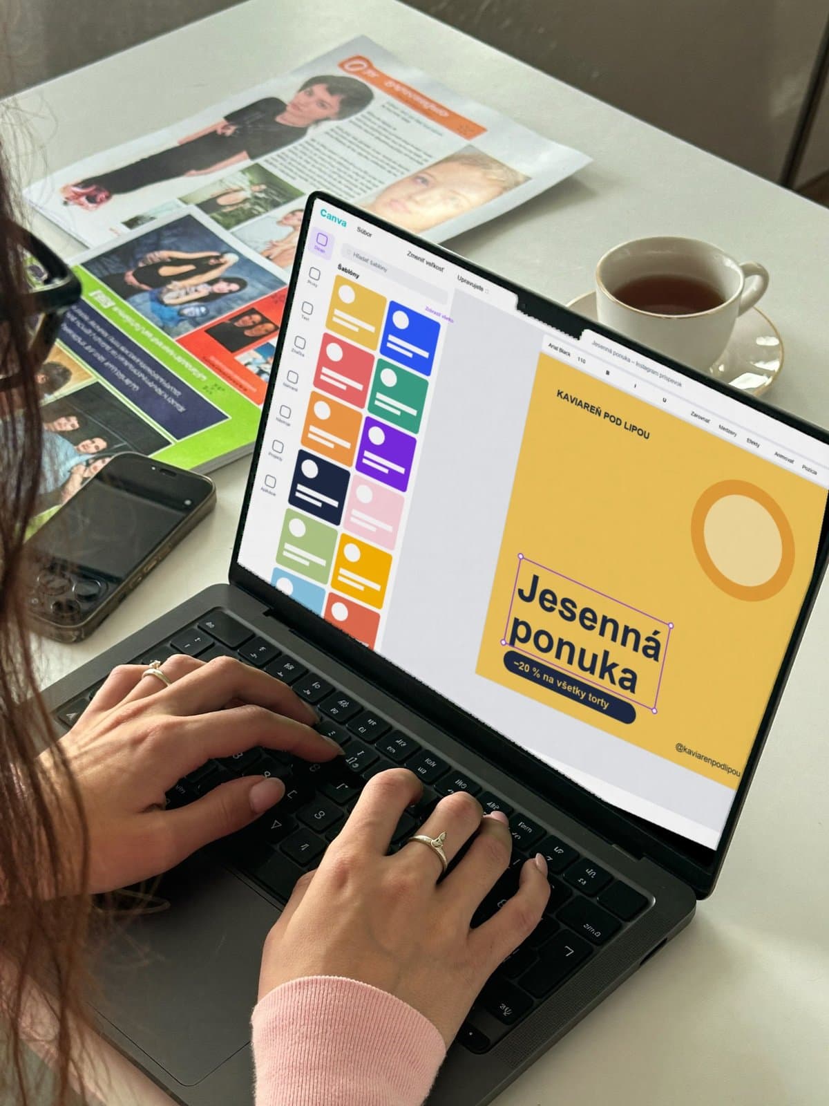 Ruky na notebooku s otvoreným editorom Canva a vytlačenými letákmi